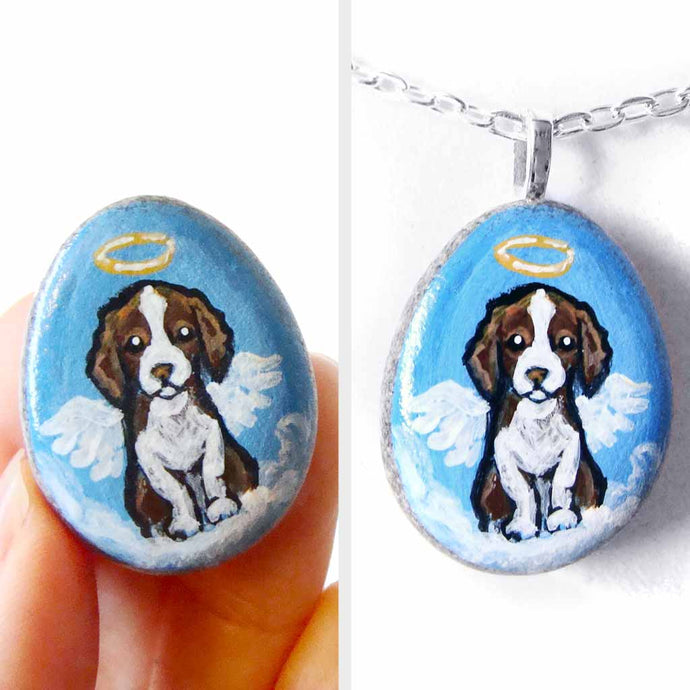 a small beach stone hand painted with a brown and white Springer spaniel dog as an angel sitting on clouds. available as a keepsake or pendant necklace