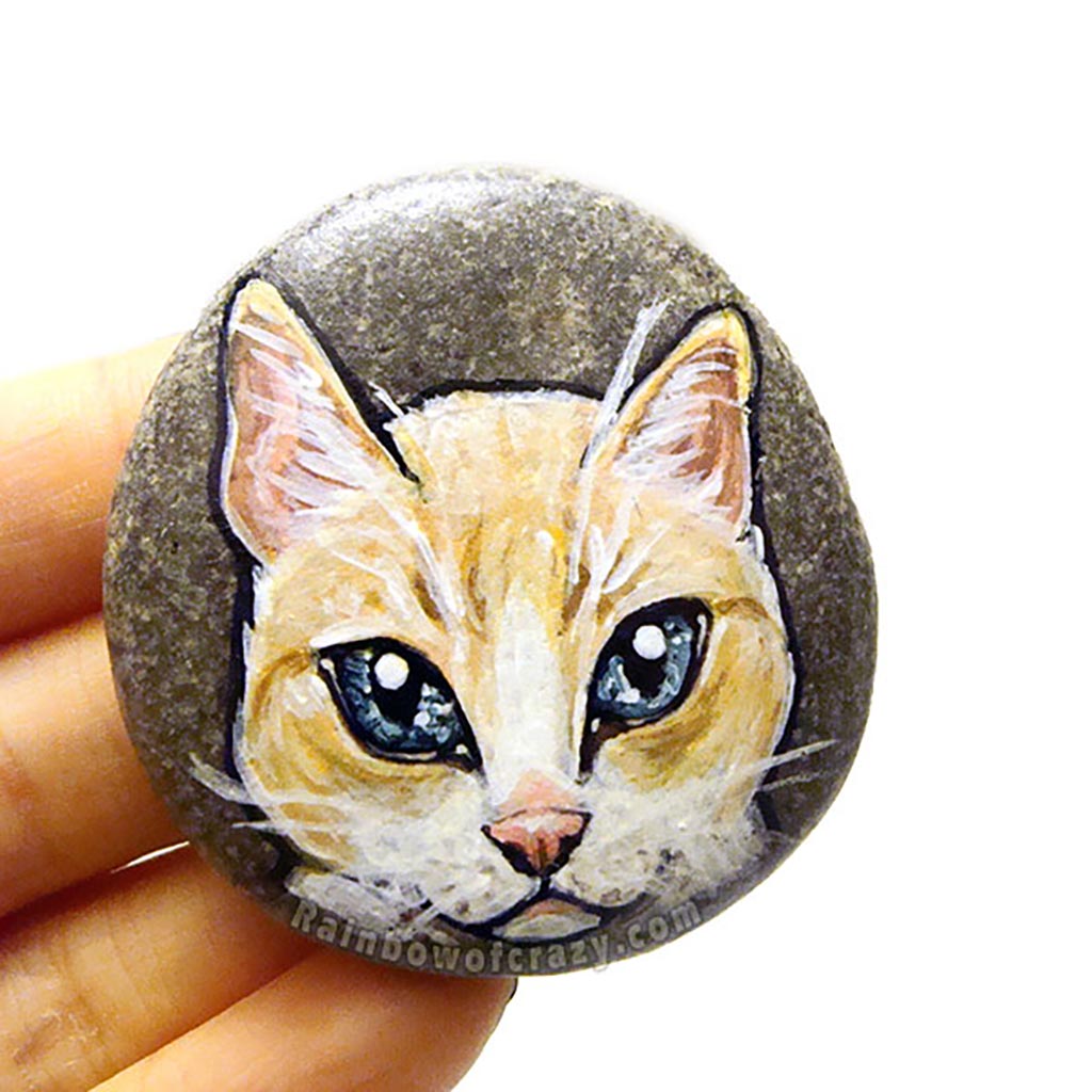 Rock art featuring the face of a flame point siamese cat with orange and white fur and grey blue eyes