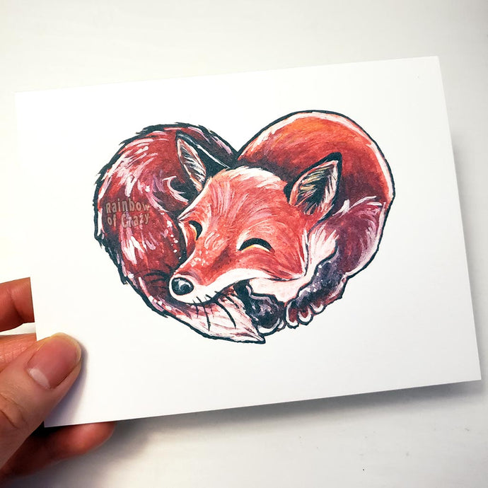 a greeting card featuring an illustration of a red fox sleeping, forming the shape of a heart.