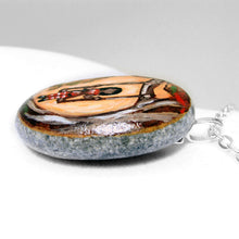 Load image into Gallery viewer, the side of a necklace handmade from a river stone and painted with a young girl in red, sitting on a tree swing
