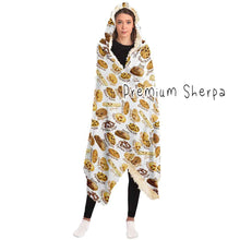 Load image into Gallery viewer, a woman wearing the Happy Cookies Hooded Blanket, featuring 10 illustrated smiling cookies patterned all over, lined with sherpa
