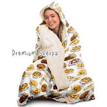 Load image into Gallery viewer, a woman wearing the Happy Cookies Hooded Blanket, featuring 10 illustrated smiling cookies patterned all over, lined with sherpa
