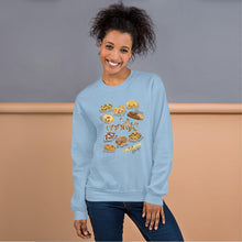 Load image into Gallery viewer, A woman is wearing the Happy Cookies Unisex Sweatshirt in the colour light blue, which features a print of 10 different types of cookies with smiley faces
