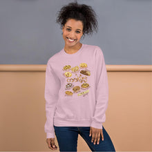 Load image into Gallery viewer, A woman is wearing the Happy Cookies Unisex Sweatshirt in the colour light pink, which features art of 10 different types of cookies with smiley faces
