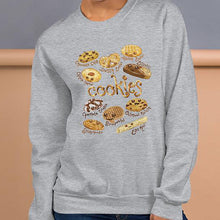 Load image into Gallery viewer, A woman is wearing the Happy Cookies Unisex Sweatshirt in the colour sport grey, which features an illustration of 10 different kinds of cookies with smiley faces
