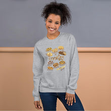 Load image into Gallery viewer, A woman is wearing the Happy Cookies Unisex Sweatshirt in the colour sport grey, which features an illustration of 10 different kinds of cookies with smiley faces
