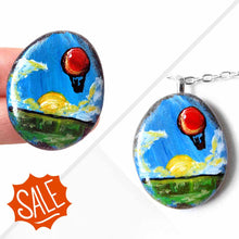 Load image into Gallery viewer, a small rock art of a red hot air balloon, floatiing in the sky over a green landscape, sun shining. available as a keepsake or pendant necklace
