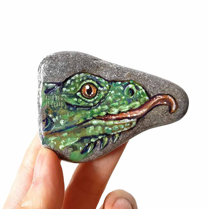 A triangle shaped stone, painted with a portrait of a green iguana