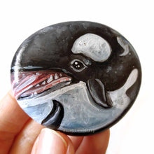 Load image into Gallery viewer, a round, flat beach stone is hand painted with art of an orca whale
