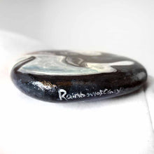 Load image into Gallery viewer, a round, flat beach stone is hand painted with art of an orca whale. it is signed in the edge with, Rainbow of Crazy
