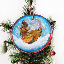 Load image into Gallery viewer, A Christmas ornament with a painting of a chicken, sitting on snow as snowflakes fall. The ornament is painted in blues and reds.

