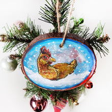 Load image into Gallery viewer, A holiday ornament with artwork of a chicken, sitting on snow as snowflakes fall. The ornament is painted in blues and reds.
