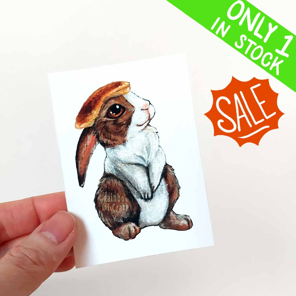 an aceo of a brown and white Dutch rabbit with a pancake on its head 