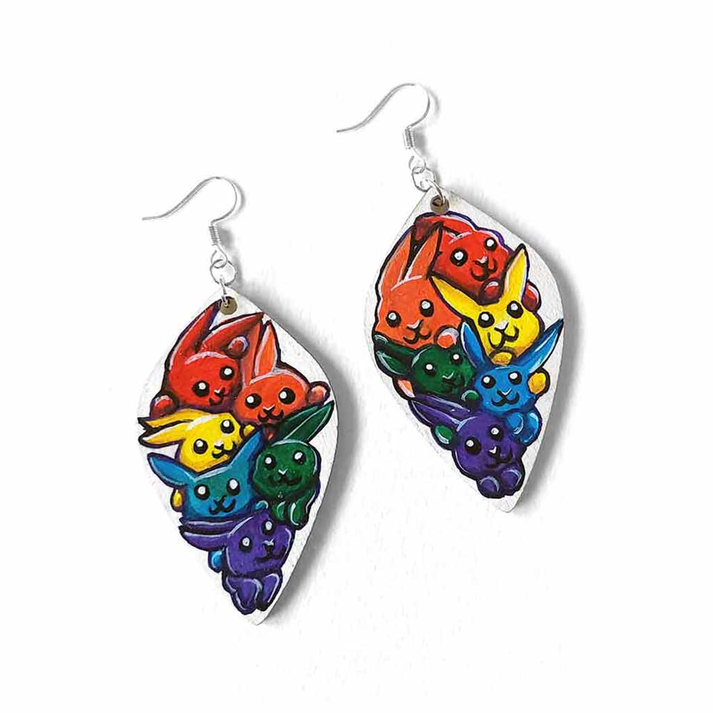 large, leaf shaped, wood earrings, hand painted with 6 cartoon style rabbits in every colour of the rainbow, against a white background.