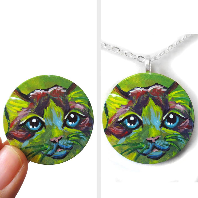 A wood pendant painted with the face of a Ragdoll cat. Available as a wood keepsake or necklace.