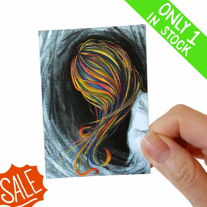 an aceo art print features the back of a woman with flowing rainbow hair, surrounded by darkness. 