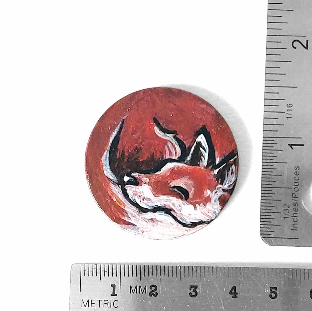 a small wood circle, hand painted with art of a red fox, curled up, sleeping. this piece is available as a keepsake or pendant necklace