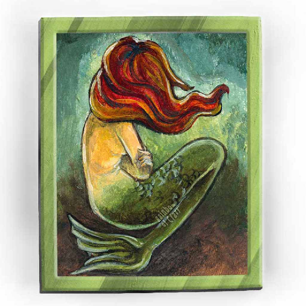 An art print of a mermaid with long red hair covering her face as she sits on the ocean floor with arms crossed