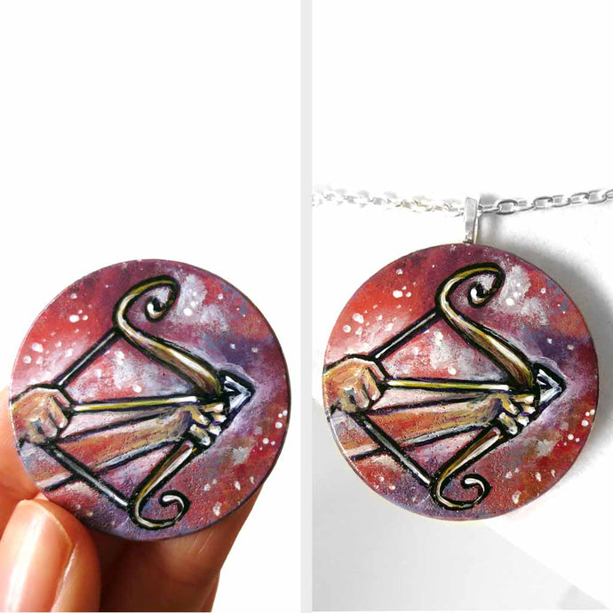 a wood circle pendant, hand painted, depicting the zodiac sign sagittarius: two hands hold a bow, with an arrow, ready to fire
