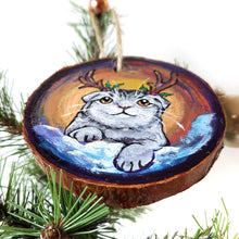 Load image into Gallery viewer, A wood Christmas ornament, hand painted with a portrait of a Scottish fold cat with reindeer antlers, sitting on the snow.
