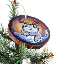 Load image into Gallery viewer, A wood Christmas ornament, hand painted with a portrait of a Scottish fold cat with reindeer antlers, sitting on the snow.
