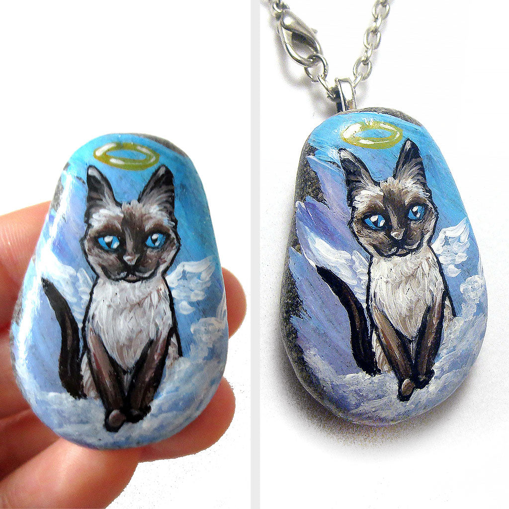 art of a siamese cat as an angel, is hand painted on a river rock, and is available as either a keepsake or a pendant necklace