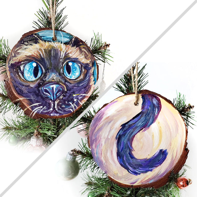 A wood ornament featuring art of a siamese cat's face with blue eyes, and it's tail on the back.
