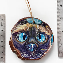 Load image into Gallery viewer, A Christmas ornament with a painting fo a blue eyed Siamese cat&#39;s face, next to two rulers to show its size: 2 15/16 x 3 1/8 inches or 7.8 x 8.4 cm
