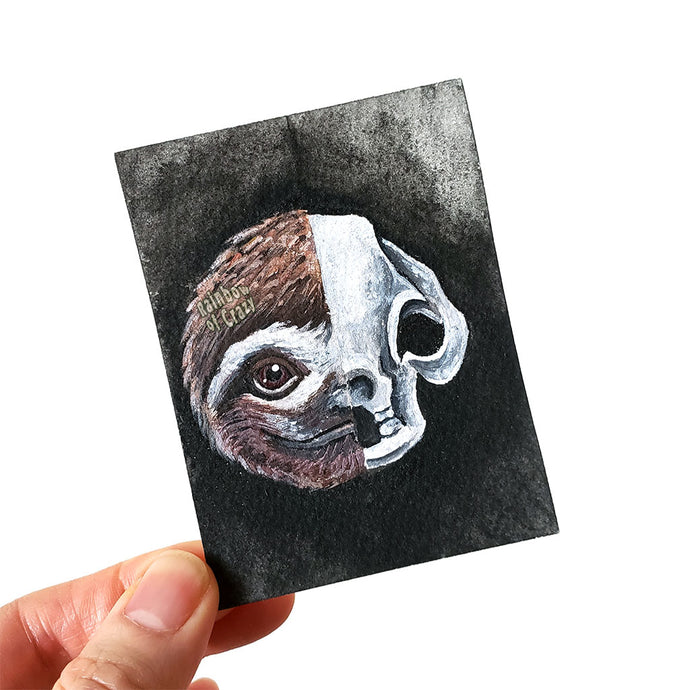 An original ACEO art card features a split portrait of a cute sloth's face on the left, and its creepy skull on the right