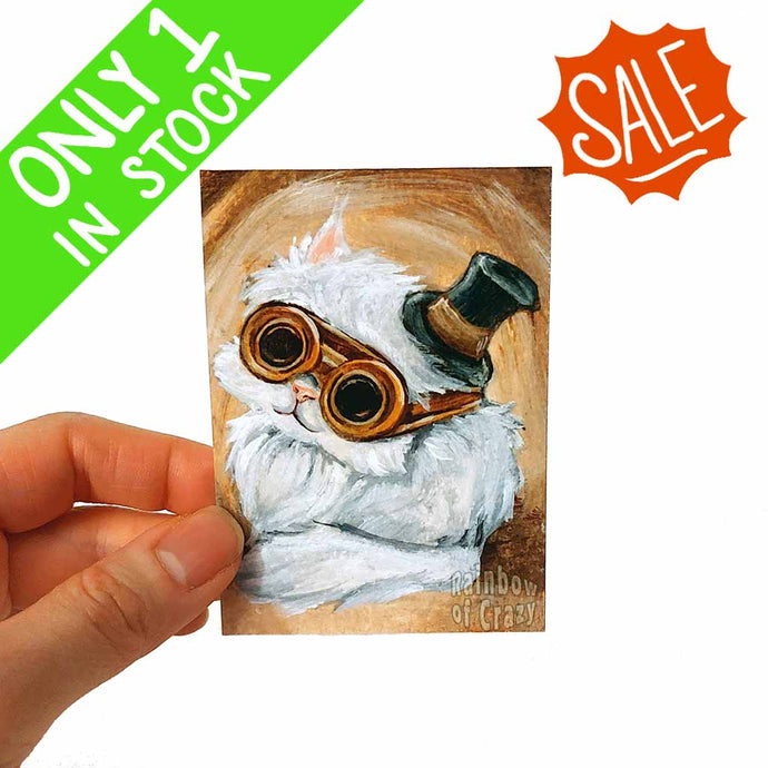 an aceo featuring a white Persian cat wearing a small top hat and steampunk goggles. 