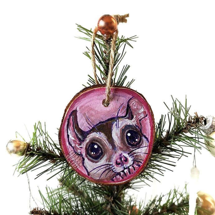 A wood Christmas tree ornament, hand painted with a painting of a sugar glider in front of a pink background.