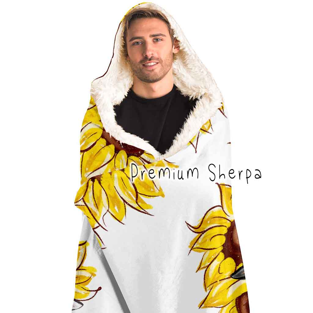 a man wears a white microfiber fleece hooded blanket, lined with premium sherpa, printed with sunflower art, with a black cat and white cat peeking out from the flowers