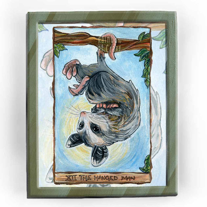 an art print of the hanged man tarot card, from the animism tarot: an opossum hangs upside down from a tree branch.