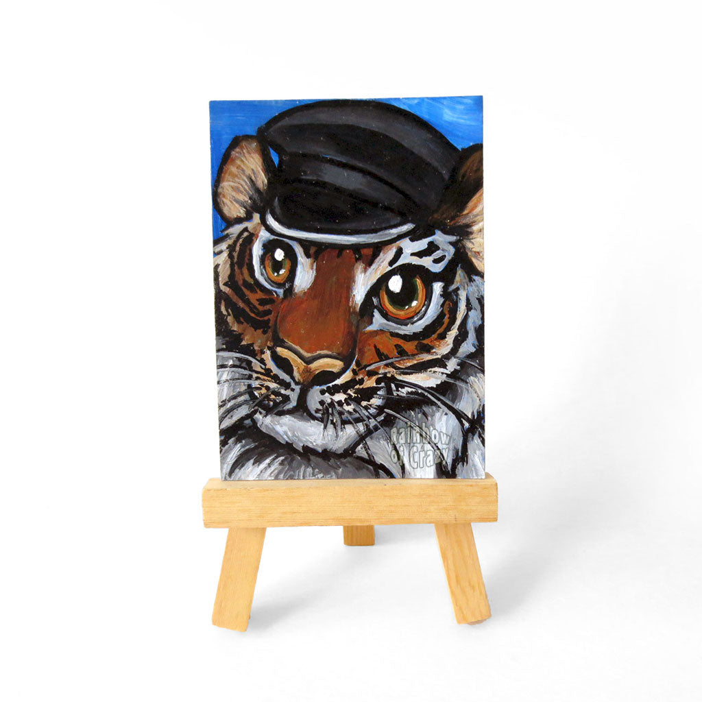 A tiger with a black leather hat, is painted on an ACEO, or 