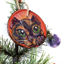 Load image into Gallery viewer, A wood Christmas tree ornament, hand painted with art of a tortoiseshell cat, with green eyes, in front of a red and pink background
