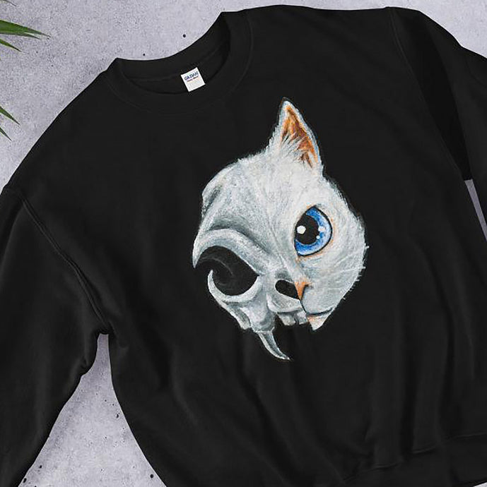 A unisex sweatshirt in the colour black, printed with art split into two: the right side features the face of a blue eyed white cat, and the left side features an evil looking cat skull.