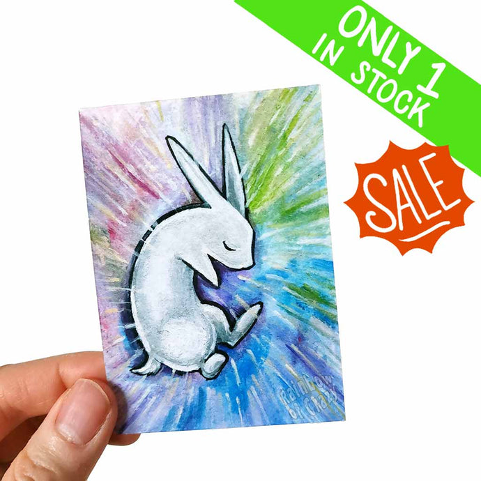 an aceo featuring a white rabbit lying on the ground with its eyes closed, surrounded by falling rain in pastel colours