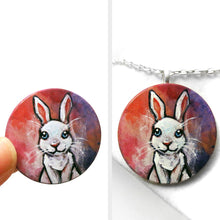 Load image into Gallery viewer, A circle wood disc painted with art of a white rabbit with blue eyes, available as a keepsake or necklace
