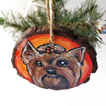 Load image into Gallery viewer, a round wood ornament, hand painted with a portrait of a Yorkshire Terrier&#39;s smiling face, against a background of red and oranges.
