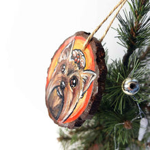 Load image into Gallery viewer, a round wood ornament, hand painted with a portrait of a Yorkshire Terrier&#39;s smiling face, against a background of red and oranges.
