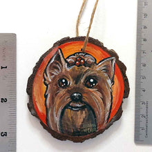 Load image into Gallery viewer, a round wood ornament, hand painted with a portrait of a Yorkshire Terrier&#39;s smiling face, against a background of red and oranges.
