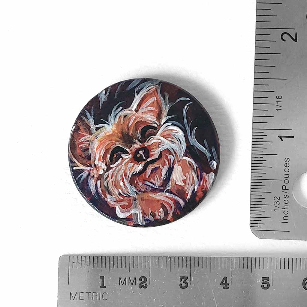 a small wood circle, hand painted with a sleeping, smiling, yorkshire terrier, available as a keepsake or pendant necklace